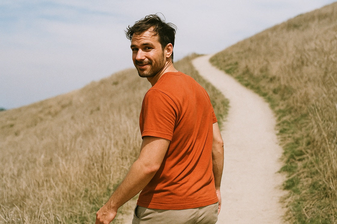 A man on a golden-grass hill trail, looking back over his shoulder